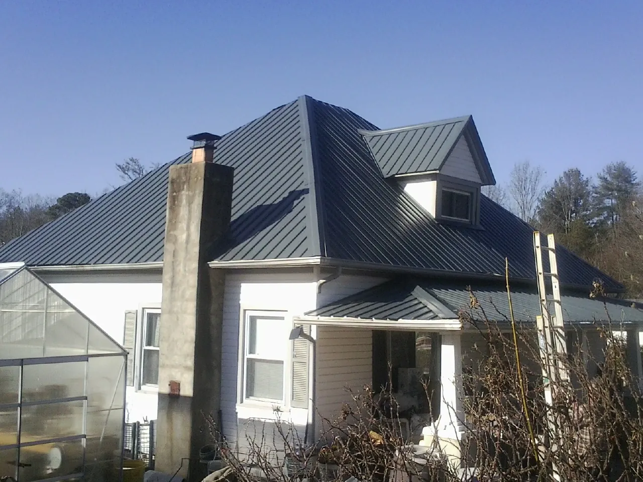 Dark blue standing seam metal roof on a white farmhouse with dormer — Slate & Tile Roof Repair by Roofing Brothers in Lester Prairie