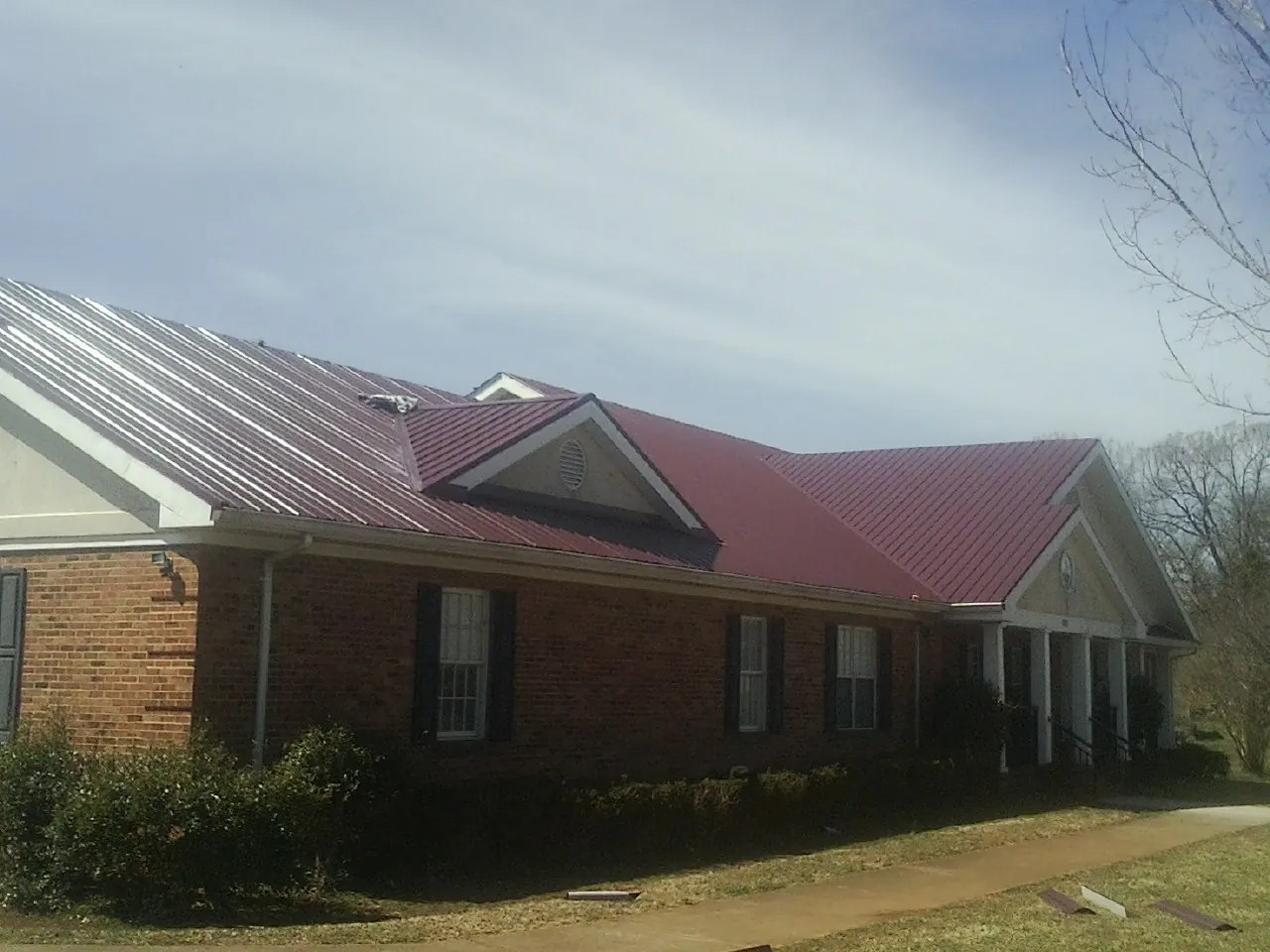 Red metal roof with gabled entries on a long brick building, from a Hail Damage Roof Repair job in Lester Prairie