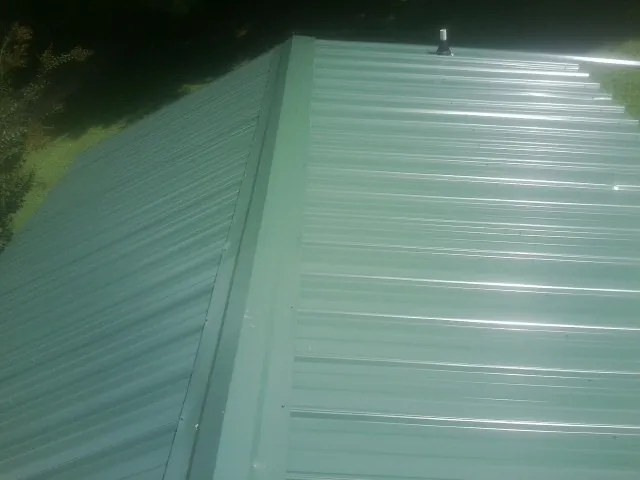 New green metal panels meeting at the ridge of a roof — Flat Roof Repair work by our crew in Lester Prairie