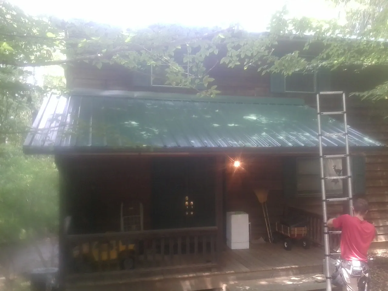 Worker on a ladder at the green porch roof of a wooded cabin in Lester Prairie