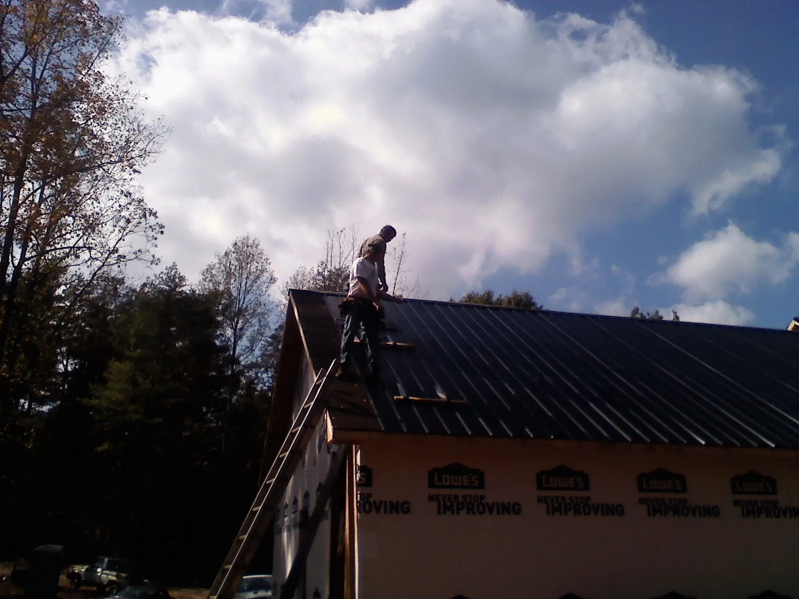 Roofer fastening dark metal panels high against a cloudy sky, from a Roof Inspection job in Lester Prairie