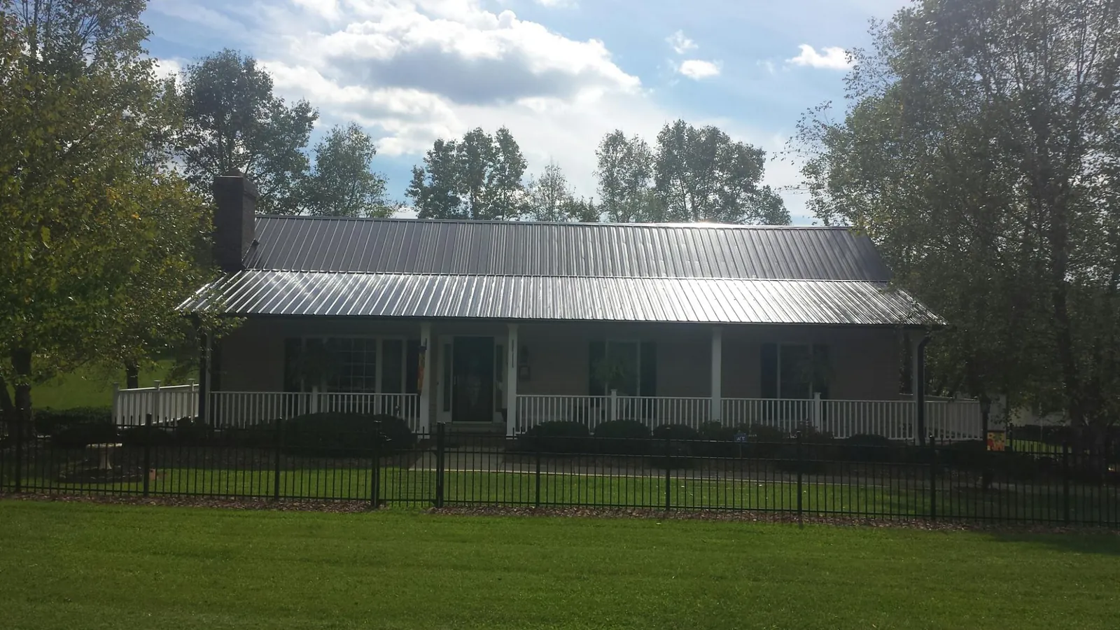 Gray metal roof on a brick ranch with a full width front porch — Gutter Guard Installation work by our crew in Lester Prairie