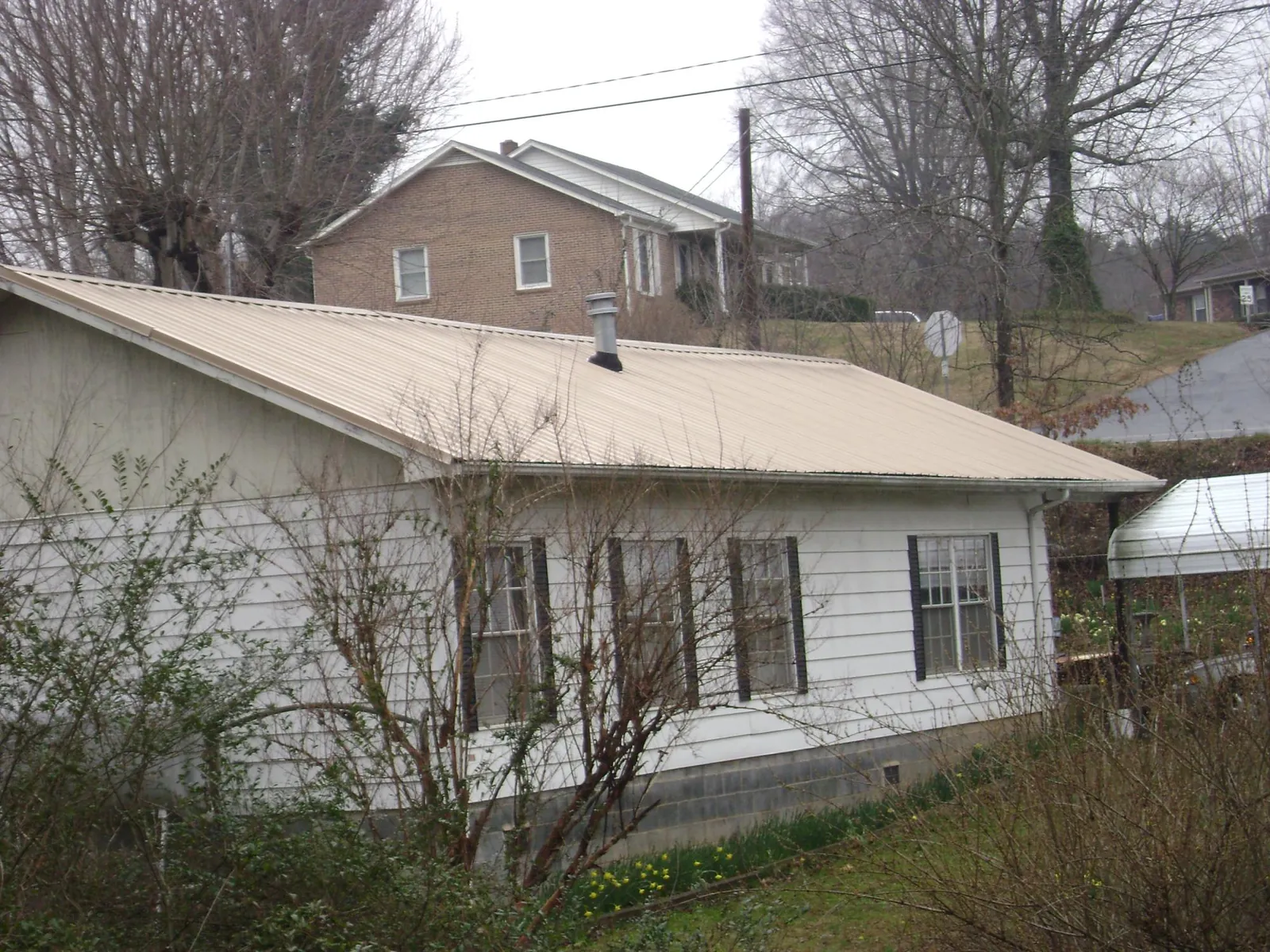 Tan metal roof on a white sided house set into a hillside — Commercial Roofing by Roofing Brothers in Lester Prairie