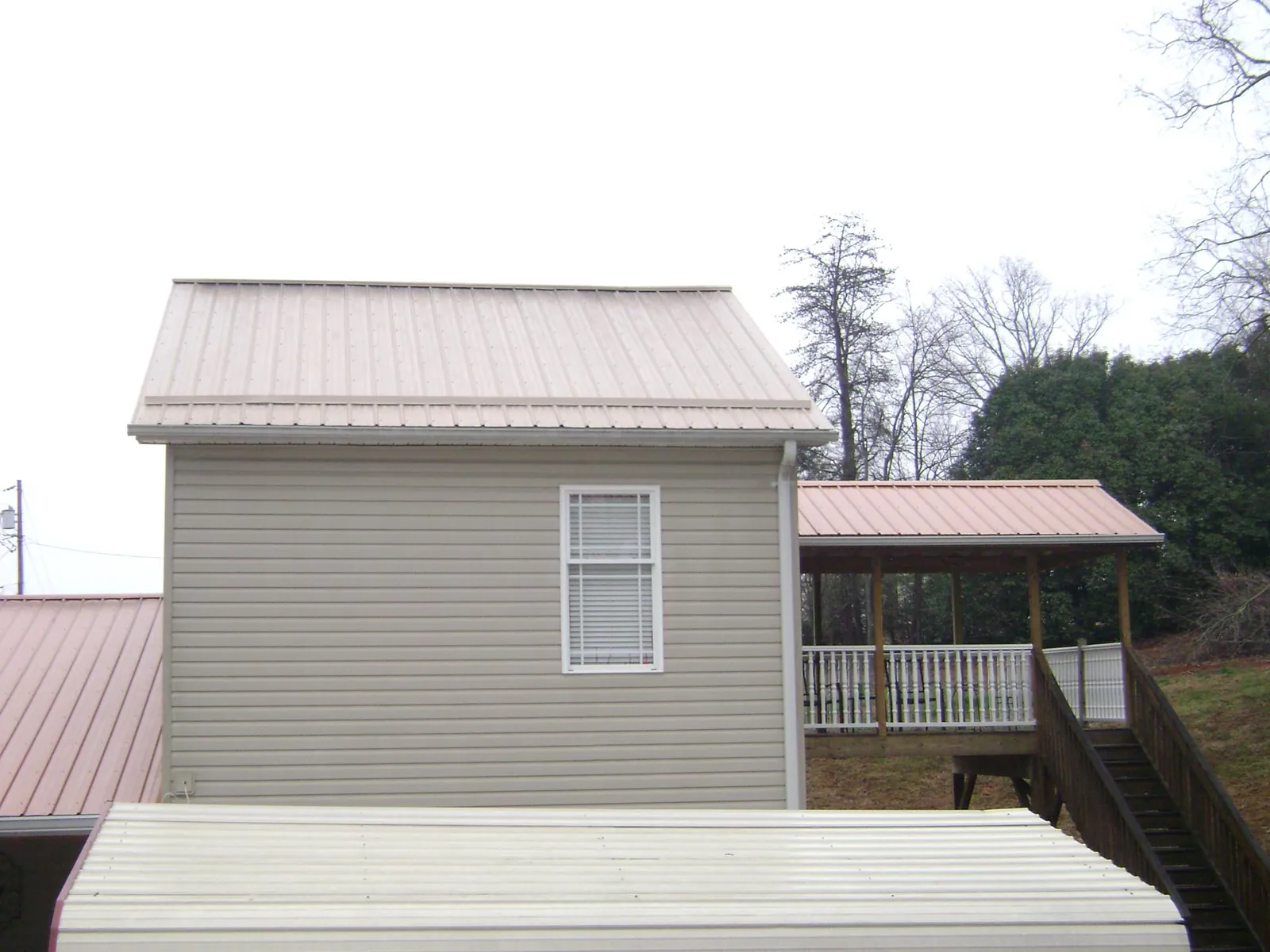 Tan metal roofs on a two story addition and attached porch, from a Roof Replacement job in Lester Prairie
